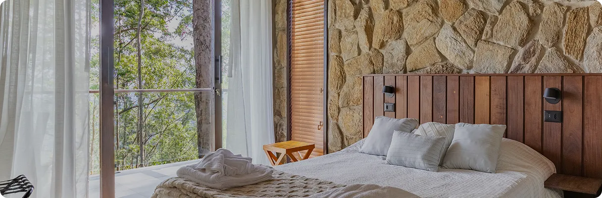 Quarto com parede de pedra e janela de vidro voltada para a mata